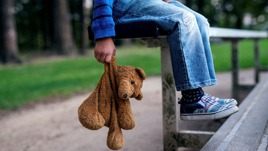 kid holding teddy bear on bench